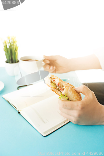 Image of The male hands holding pen and sandwich. The trendy blue desk.