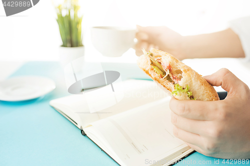 Image of The male hands holding pen and sandwich. The trendy blue desk.