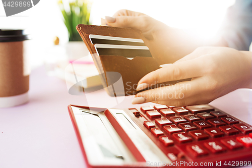 Image of woman is holding purse, credit card in hands and calculating the costs