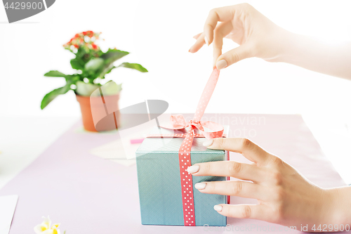 Image of Close-up of female hands holding a present. The trendy pink desk.