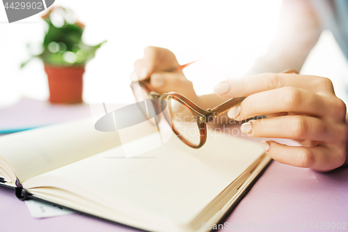 Image of The female hands holding glasses. The trendy pink desk.