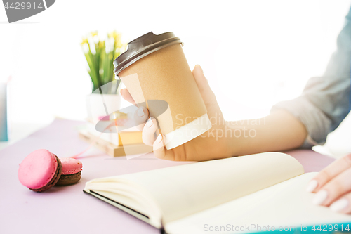 Image of The female hands holding coffee. The trendy pink desk.