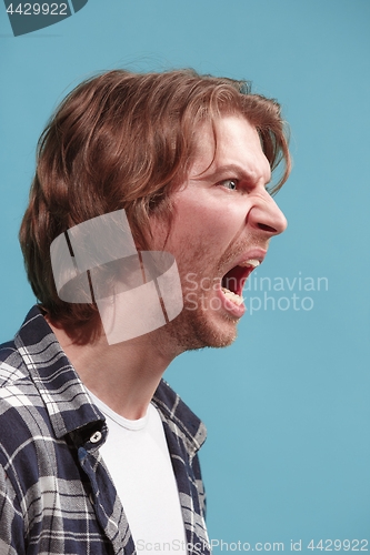 Image of The young emotional angry man screaming on blue studio background