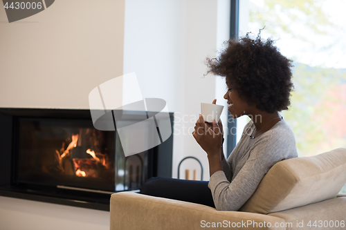 Image of black woman drinking coffee in front of fireplace