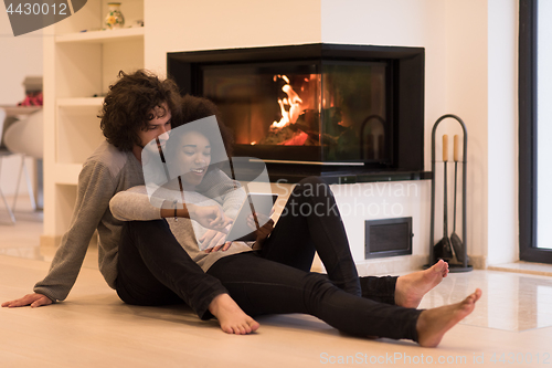 Image of multiethnic couple using tablet computer on the floor