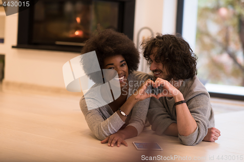 Image of multiethnic couple showing a heart with their hands on the floor