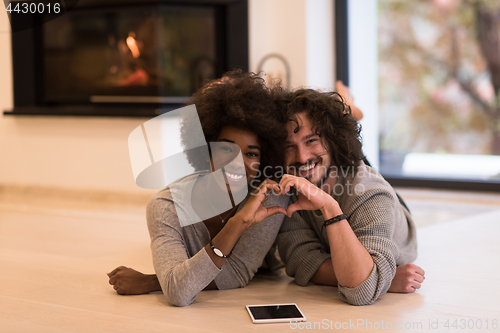 Image of multiethnic couple showing a heart with their hands on the floor