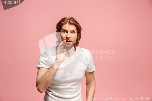 Image of The young man whispering a secret behind her hand over pink background