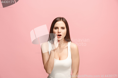 Image of The young woman whispering a secret behind her hand over pink background