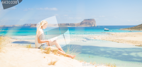 Image of Woman reading book, enjoying sun on beach.