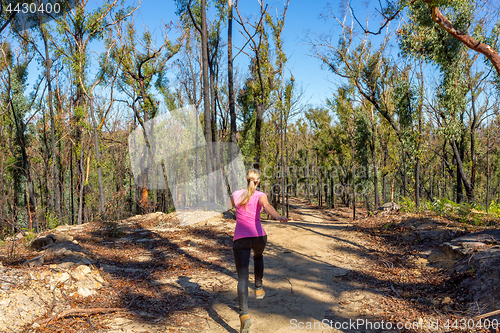 Image of Woman running along dirt trail in forest area