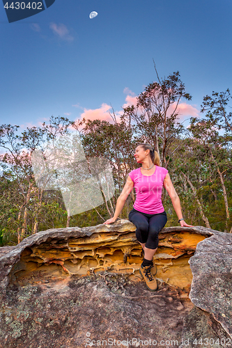 Image of Happy woman sitting on a rock with moon shining above