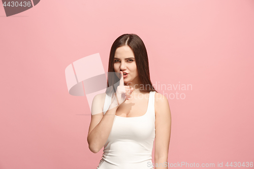 Image of The young woman whispering a secret behind her hand over pink background