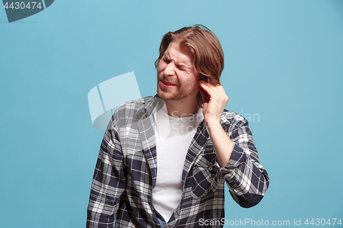 Image of The Ear ache. The sad man with headache or pain on a blue studio background.