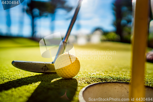 Image of Mini Golf yellow ball with a bat near the hole at sunset