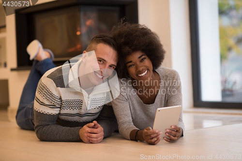 Image of multiethnic couple using tablet computer on the floor