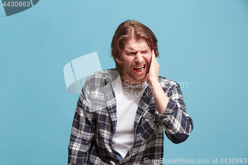 Image of The Ear ache. The sad man with headache or pain on a blue studio background.