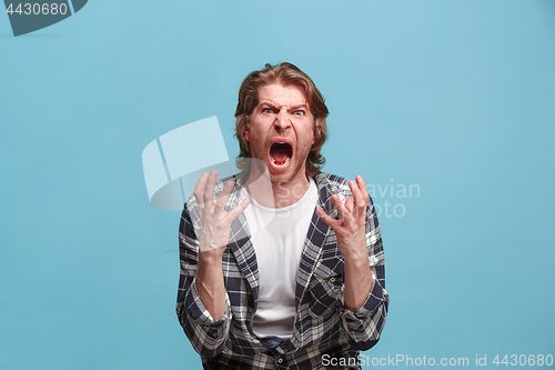 Image of The young emotional angry man screaming on blue studio background