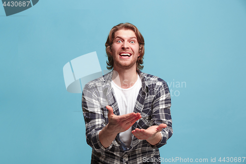 Image of male half-length portrait isolated on blue studio backgroud. The young emotional surprised man