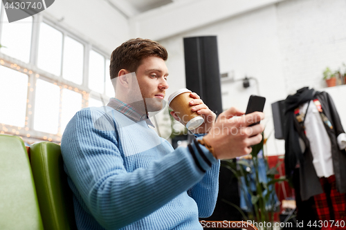 Image of man with smartphone and coffee at clothing store