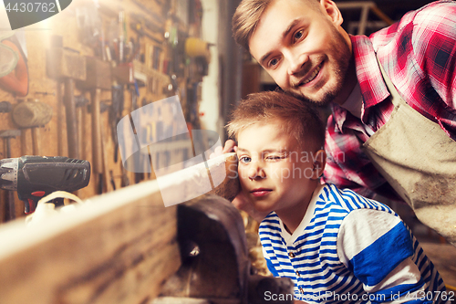 Image of father and little son with wood plank at workshop