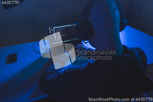 Image of hacker with coding on laptop computer in dark room