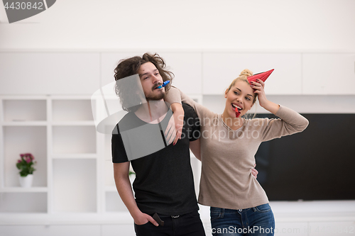 Image of couple in party hats blowing in whistle