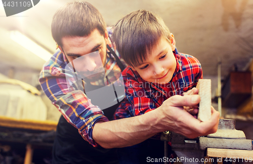 Image of father and little son with wood plank at workshop