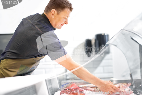 Image of male seller with seafood at fish shop fridge