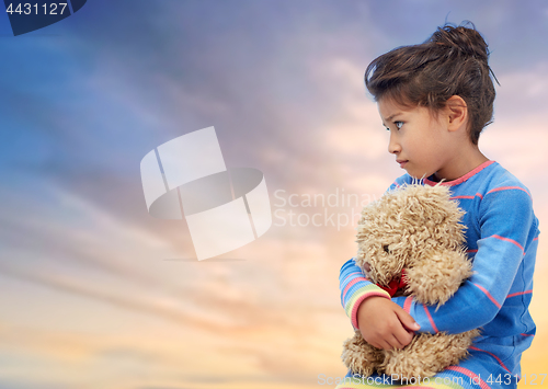 Image of sad little girl with teddy bear over evening sky