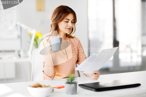 Image of businesswoman with papers drinks coffee at office