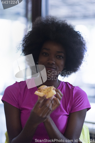 Image of woman with afro hairstyle eating tasty pizza slice