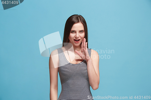 Image of The young woman whispering a secret behind her hand over blue background