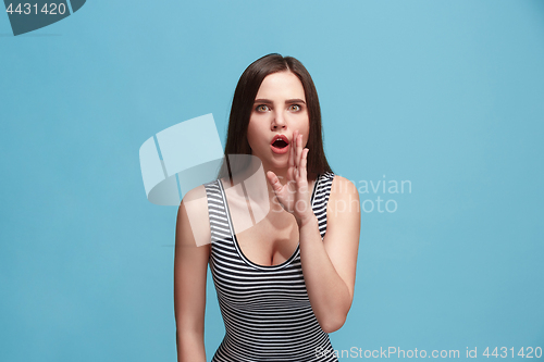 Image of The young woman whispering a secret behind her hand over blue background