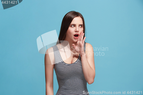 Image of The young woman whispering a secret behind her hand over blue background