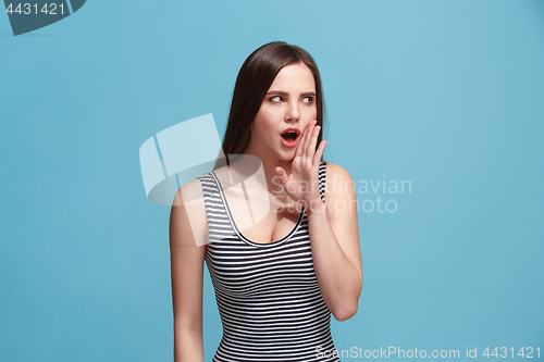 Image of The young woman whispering a secret behind her hand over blue background