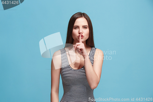 Image of The young woman whispering a secret behind her hand over blue background