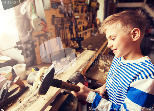 Image of happy little boy with hammer and plank at workshop