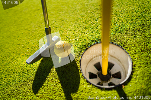 Image of Mini Golf yellow ball with a bat near the hole at sunset