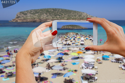 Image of Young girl with mobile phone photographs Cala Conta beach in Ibi