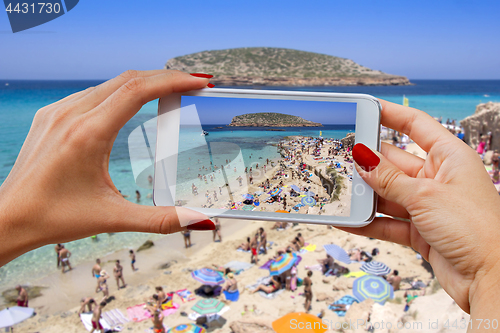 Image of Young girl with mobile phone photographs Cala Conta beach in Ibi