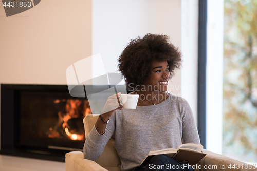 Image of black woman reading book  in front of fireplace