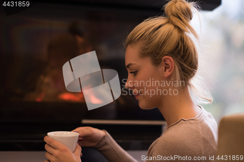 Image of young woman drinking coffee in front of fireplace