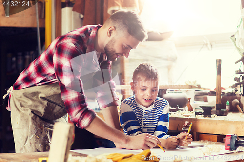 Image of happy father and son with blueprint at workshop