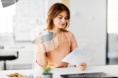 Image of businesswoman with papers drinks coffee at office