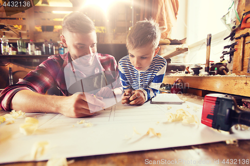 Image of happy father and son with blueprint at workshop