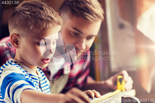 Image of father and son with ruler measure wood at workshop