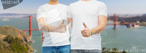 Image of gay couple with rainbow wristbands shows thumbs up