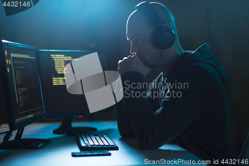 Image of hacker with coding on laptop computer in dark room
