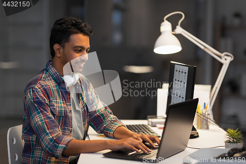 Image of creative man with laptop working at night office